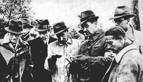 Zdjęcie przedstawiające mężczyzn w kapeluszach, ubranych w płaszcze przeglądających dokumenty. Są to członkowie międzynarodowej delegacji wizytujący miejsce ekshumacji w Katyniu w 1943 roku