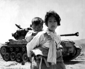 Koreańska dziewczynka z młodszym bratem na plecach, w tle czołg amerykański M-46 Patton, Haengju, Korea, czerwiec 1951. Zdjęcie z domeny publicznej rządu USA