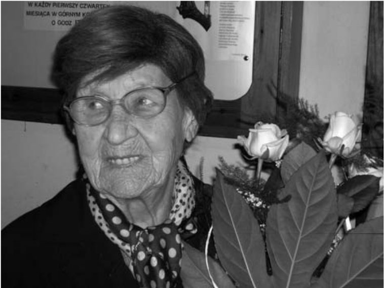 Czarno-białe zdjęcie, starsza kobieta trzyma bukiet kwiatów.