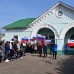 Młodzież z flgami i transparentami w barwach Polski i Rosji na tle budynku stacji kolejowej.