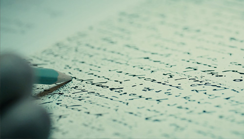 Zdjęcie na którym widać rękę trzymającą ołówek, który wskazuje na trudne do odczytania pismo na kartce papieru. Kadr z filmu "Sztafeta", Narodowe Centrum Kultury 2018