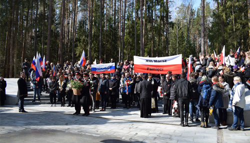 Młodzież z flgami i transparentami w barwach Polski i Rosji, w tle las.