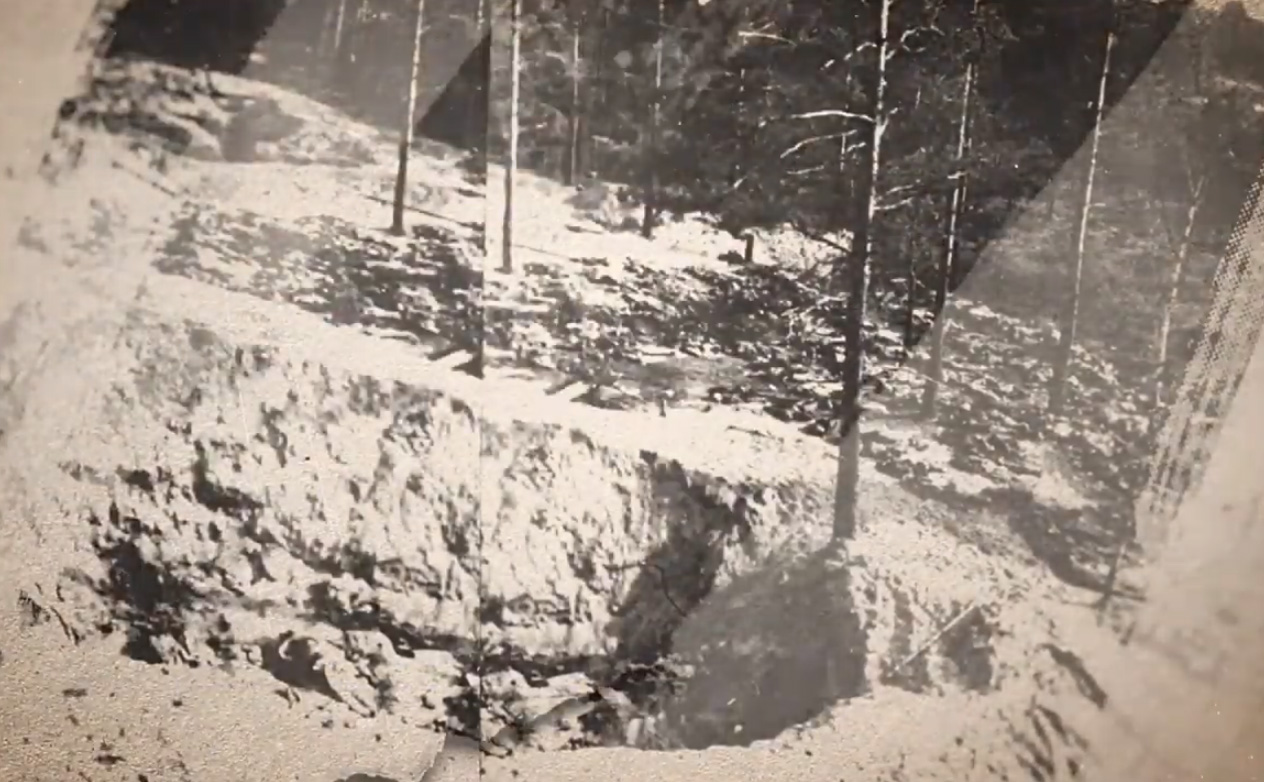 Fotografia przedstawiająca odkopany dół ze szczątkami polskich oficerów w trakcie ekshumacji w 1943 roku w Katyniu. W tle widać młody las sosnowy.